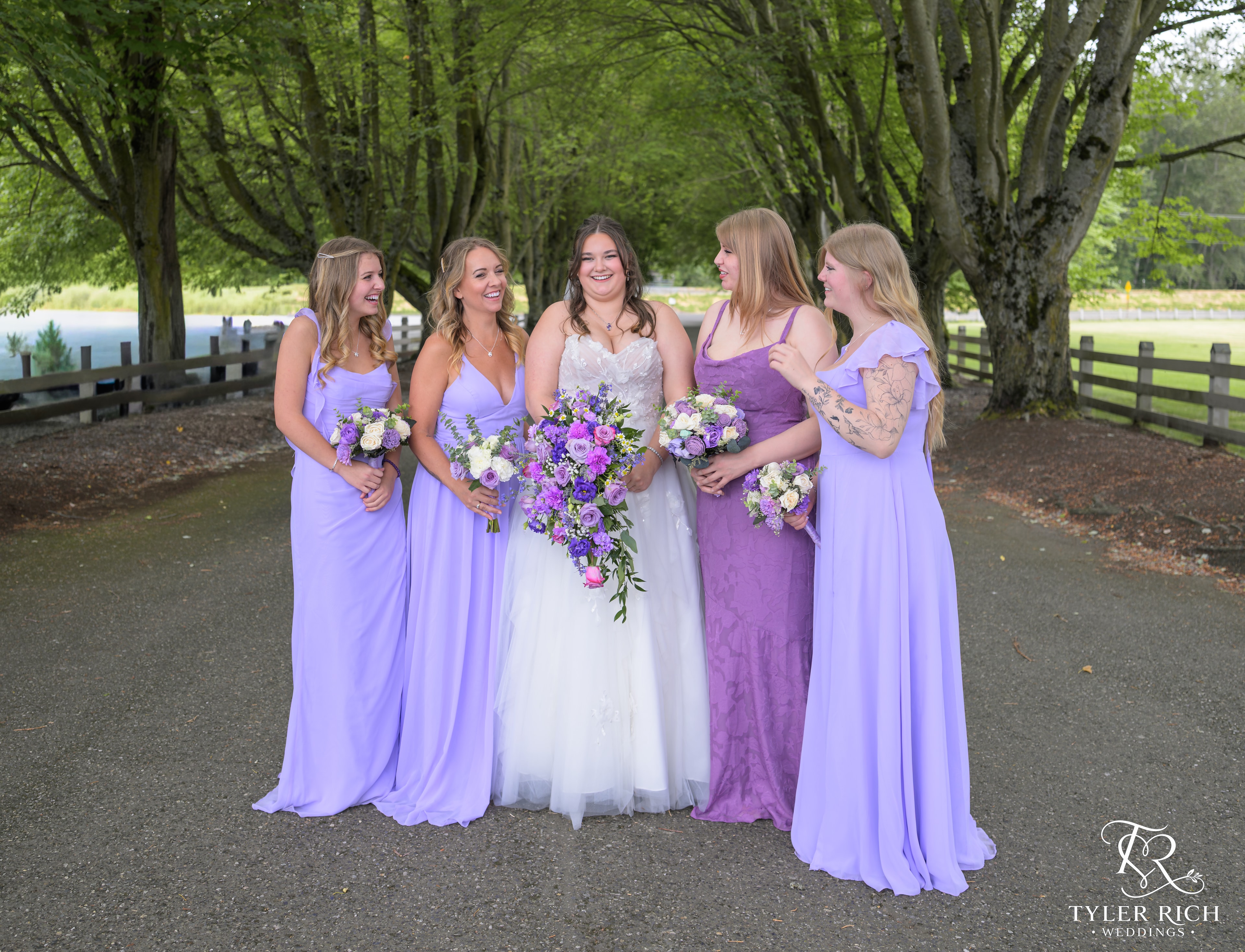 Bride and bridesmaids in purple dresses on a tree-lined path