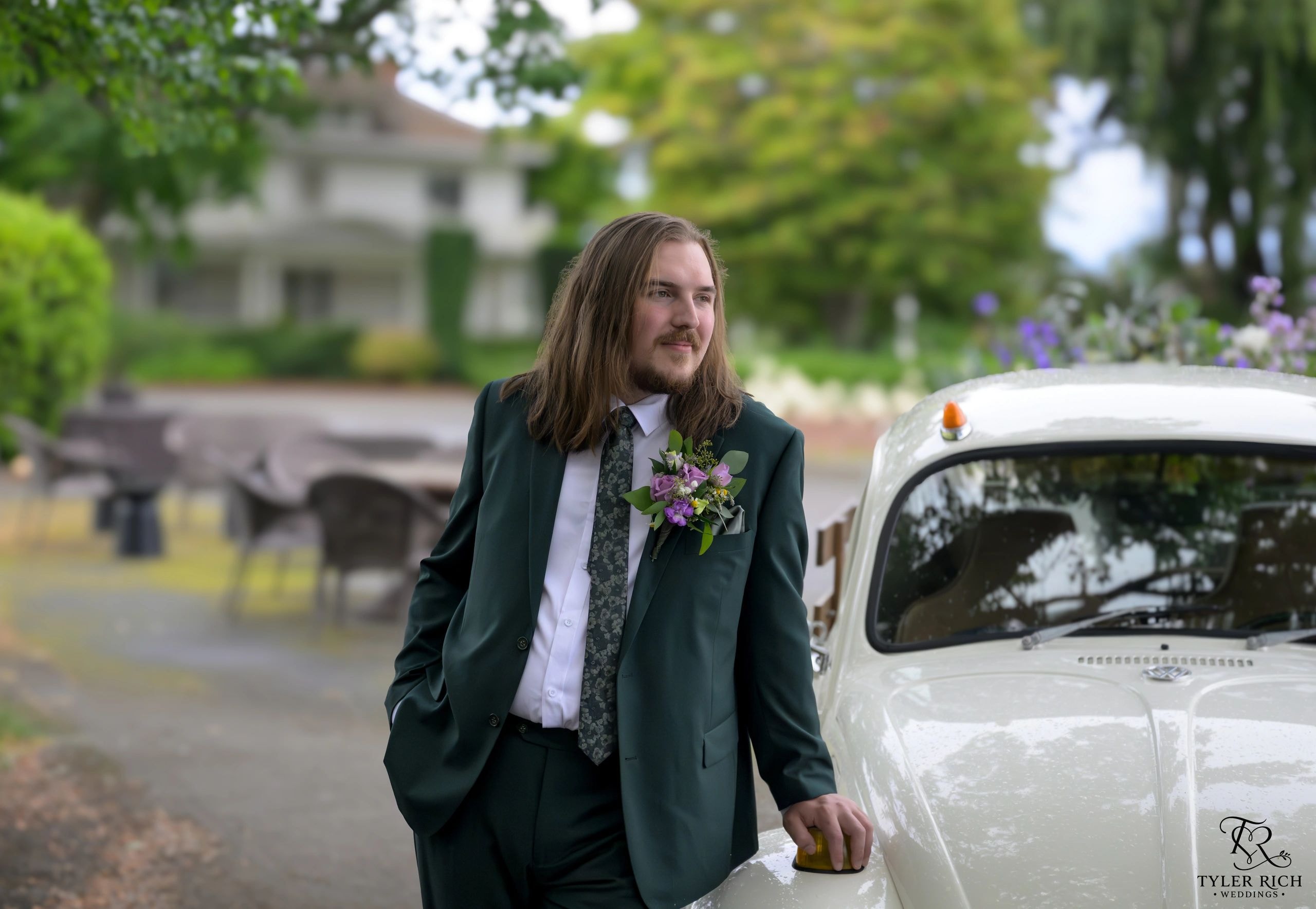 Groom in green suit beside a vintage car in a garden