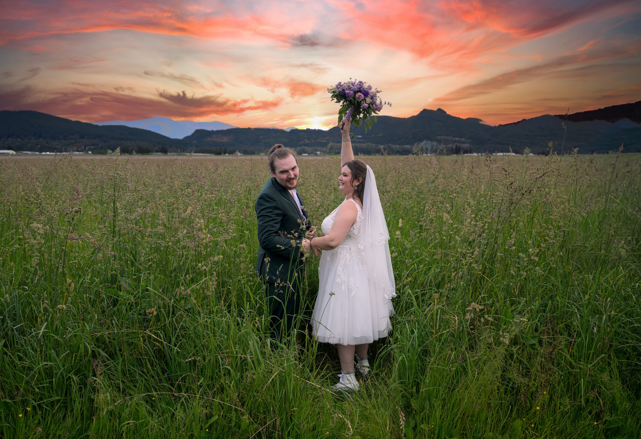Newlyweds holding a bouquet in a meadow at sunset