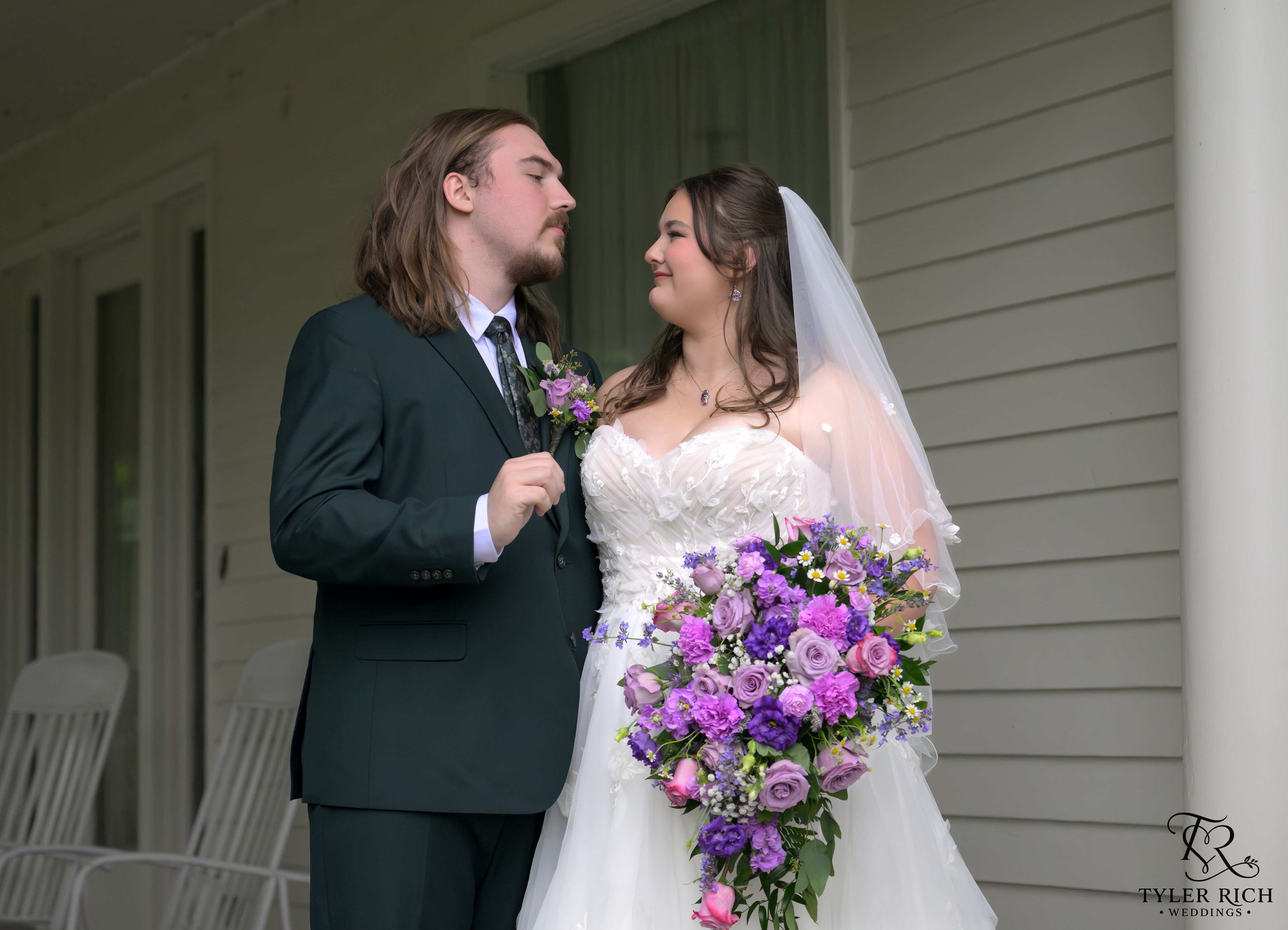 Bride and groom on a porch with a purple cascading bouquet